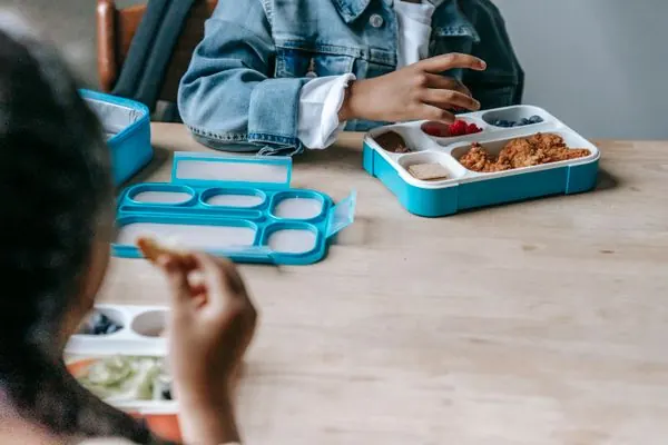 Children enjoying colorful compartmented lunch boxes with healthy food