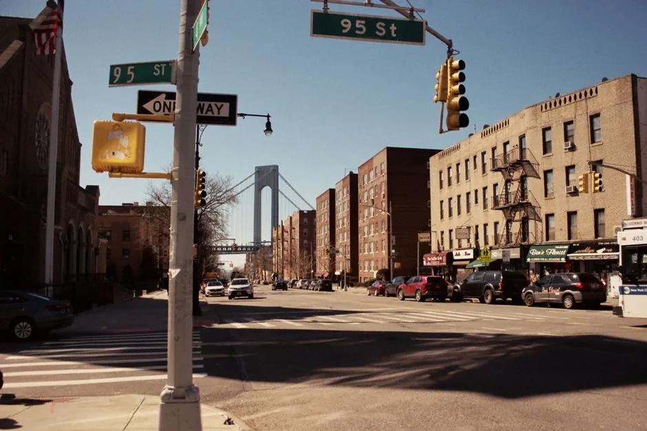A Bay Ridge Brooklyn street corner with parked cars and the Verrazzano-Narrows Bridge in the background