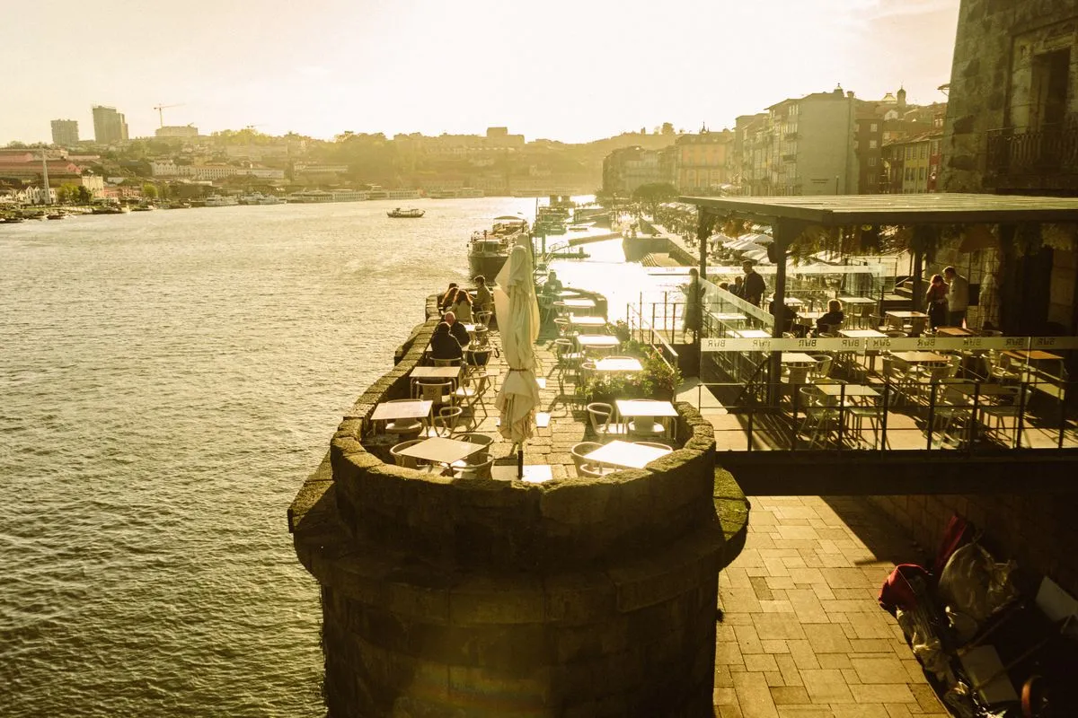 Outdoor cafe seating along a waterfront promenade at golden hour, similar to the Bay Ridge Brooklyn waterfront dining experience